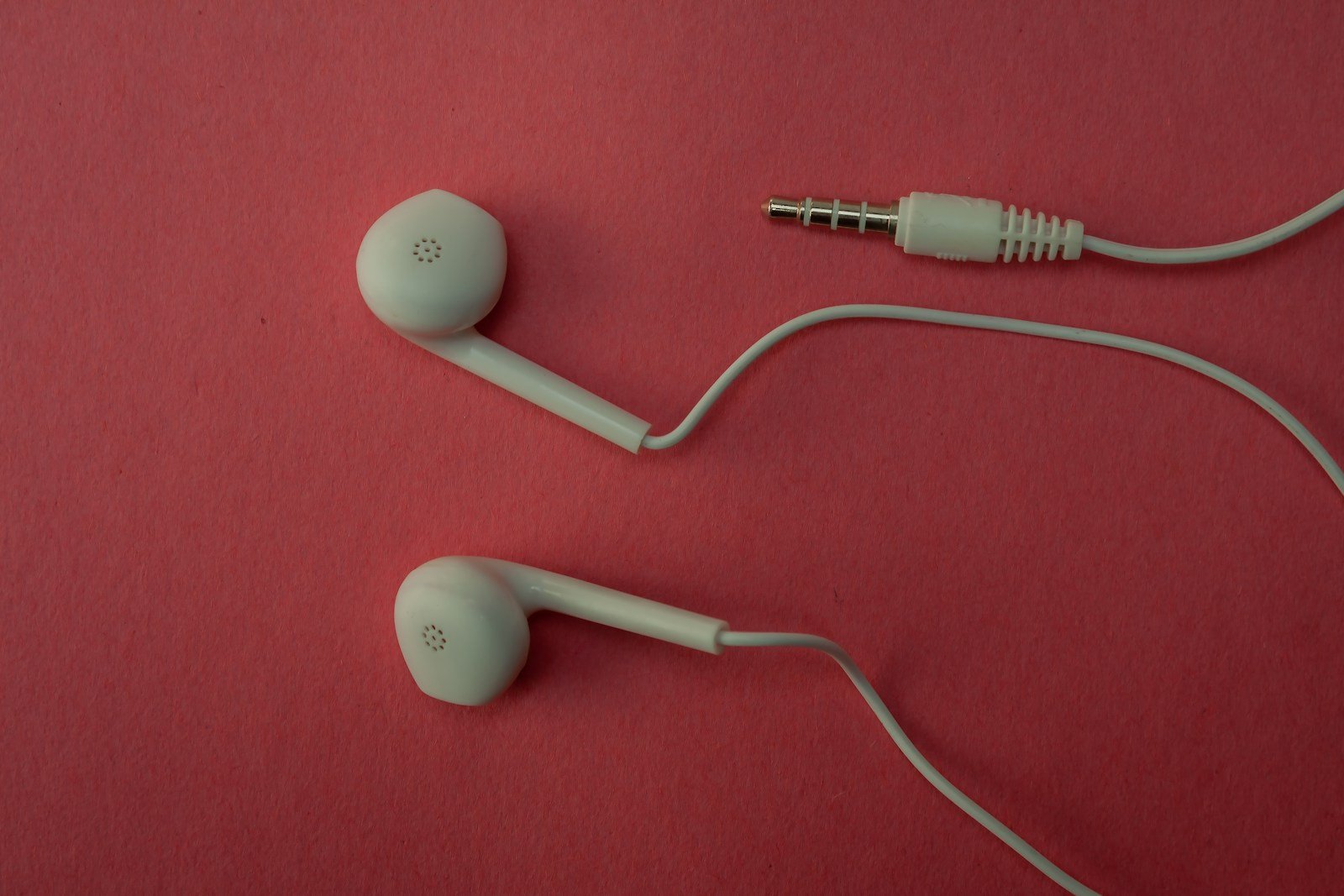 White earbuds and their cable on a pink surface.